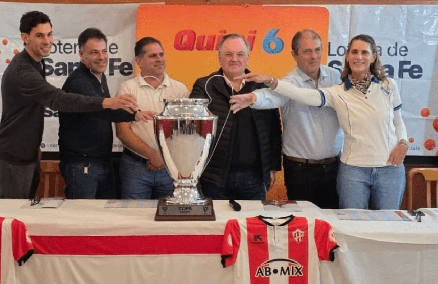 Felipe Michlig, Marcelo González y Carlos Lanzaro sostienen la Copa Santa Fe durante la presentación oficial en Suardi junto a autoridades.